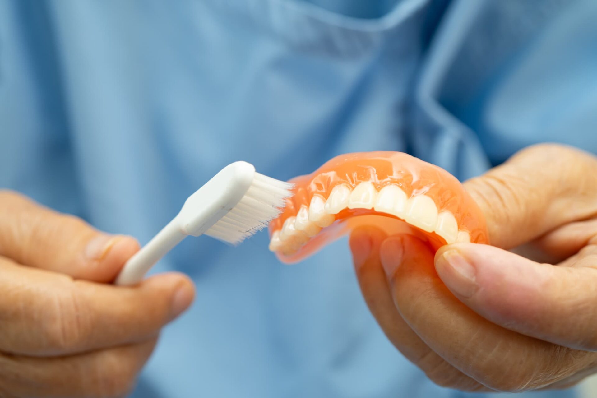 入れ歯を歯ブラシで洗っている人の手元