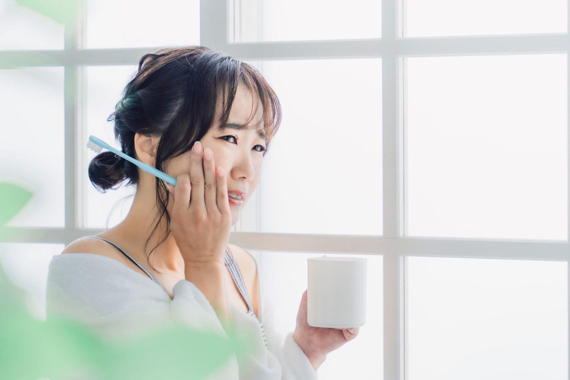歯磨き時に歯がしみて頬を押さえる女性